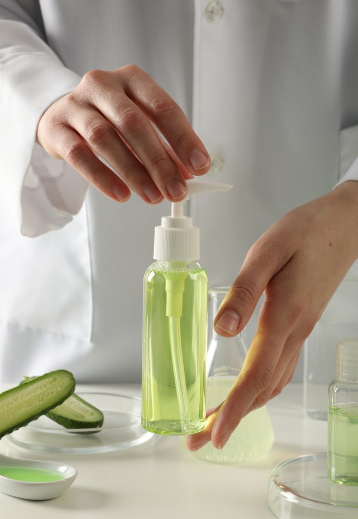 Sliced cucumber and flasks with cosmetics, female hands of laboratory assistant